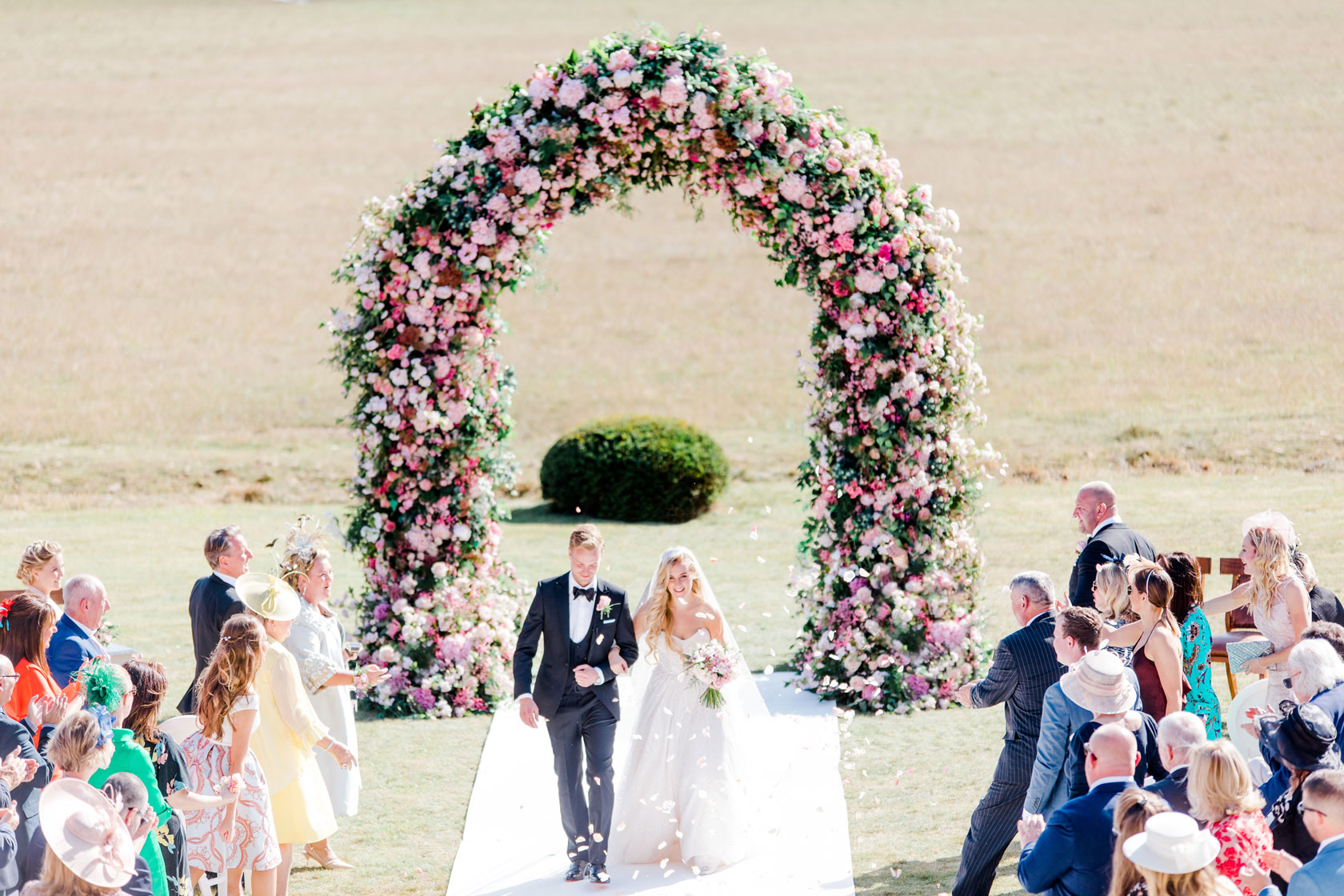 Bride and Groom walking down the aisle outdoors with a beautiful flower arch behind them