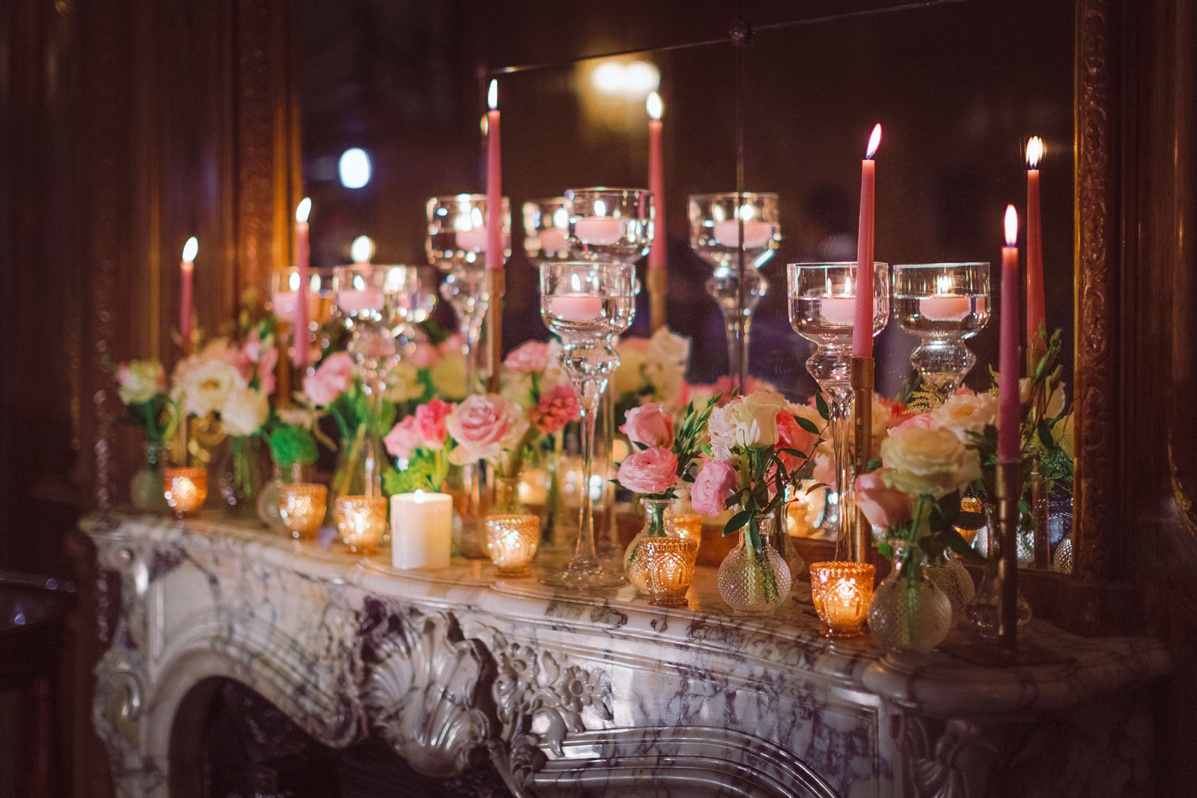 marble mantelpiece inside Claridges decorated with flowers in glass vases and lit candles for a wedding