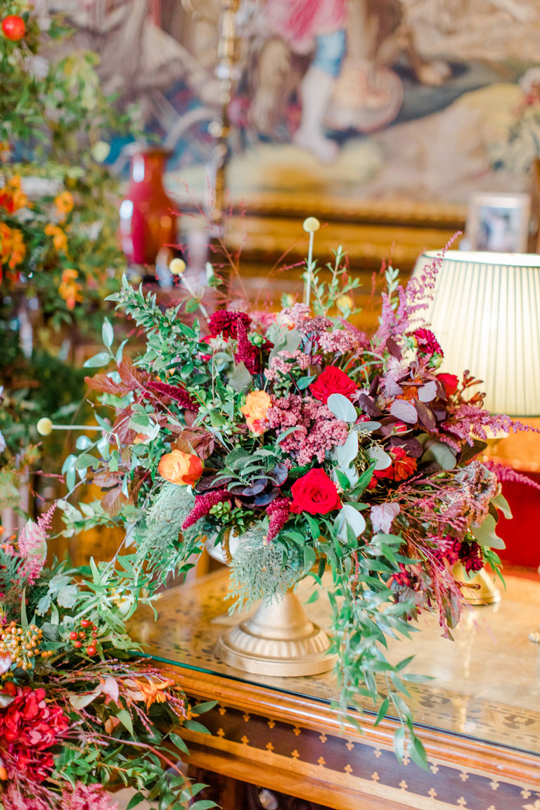 table flowers of oranges, browns, rich reds in a gold urn