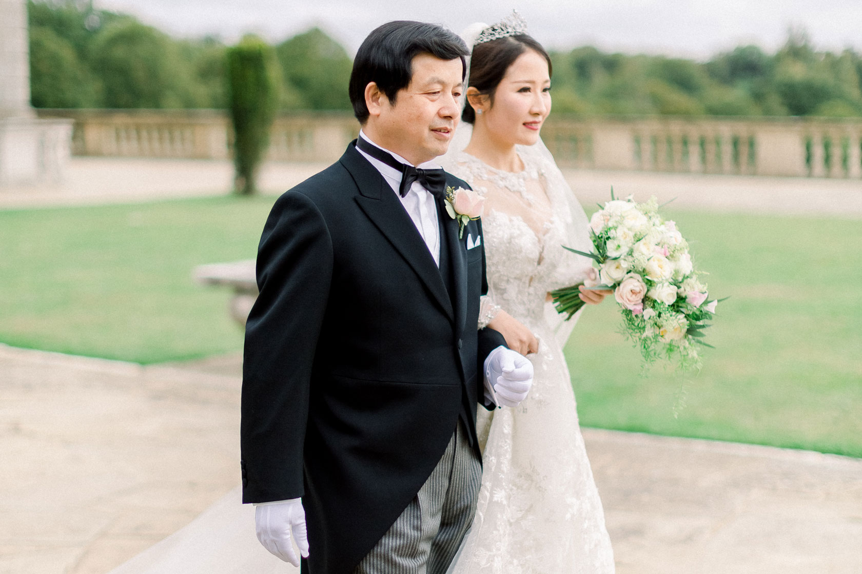 Chinese bride with her Father walking down the aisle with her bridal bouquet on the lawn at Cliveden House