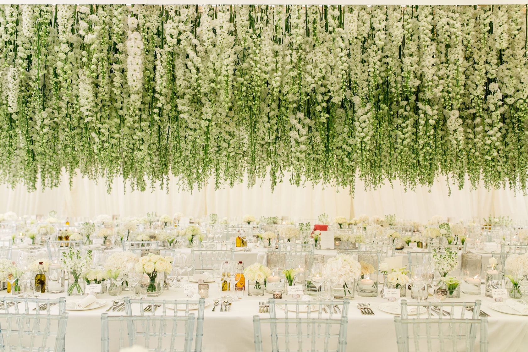 thousands of white delphiniums hanging over a table inside a marquee for a white wedding