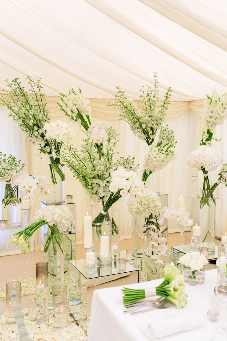 glass vases with white flowers on mirrored plinths and candles inside a marquee